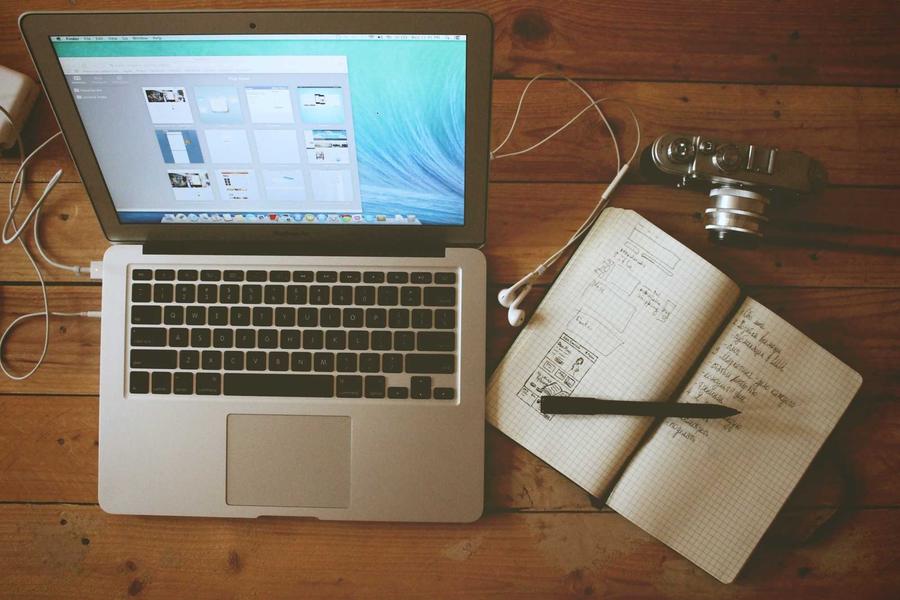 An open laptop beside a notebook with notes and a pen