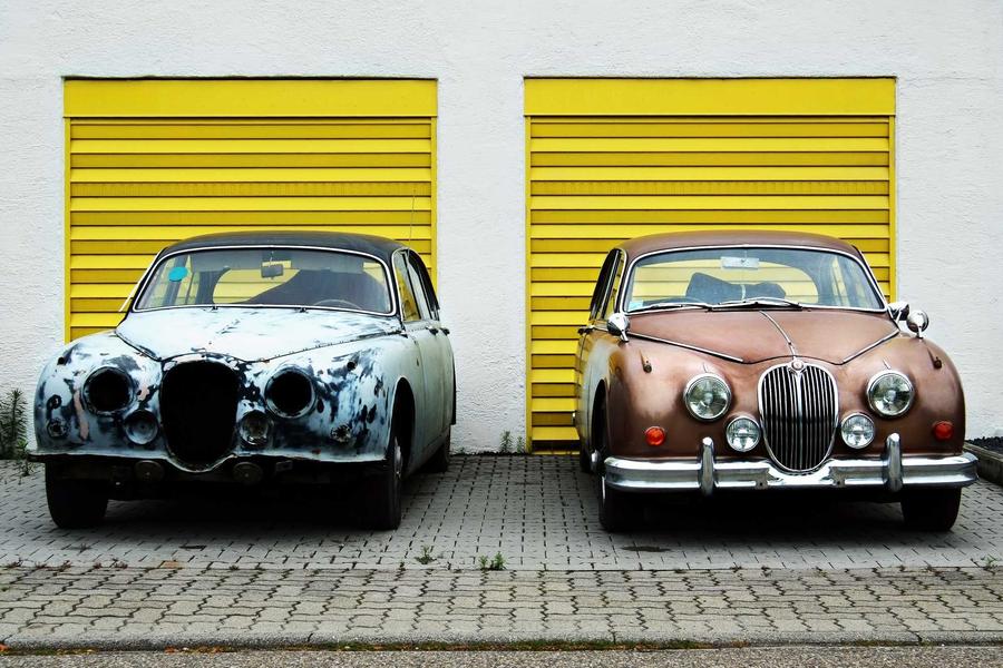 Two classic cars parked side by side in front of two identical garage doors